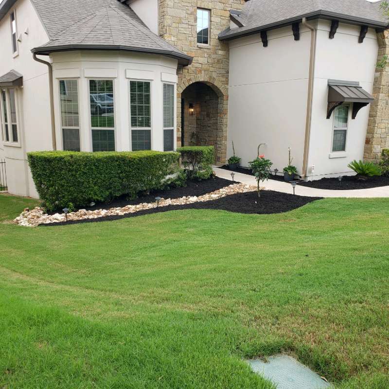 Manicured lawn and planting bed in front of a Hill Country stone home