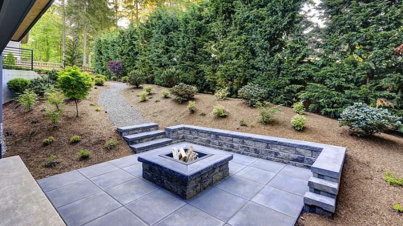 Stone fire pit and paver patio with built-in seat wall in a landscaped Austin backyard